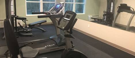 Un gimnasio con cinta de correr, banco de pesas y varias máquinas de ejercicio.