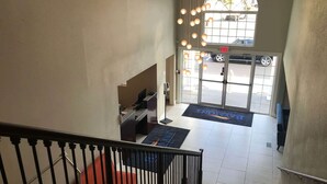 A hotel reception area with a staircase, a reception desk, a large window, and a door leading outside. - Baymont by Wyndham Lake Park Valdosta I-75 (Lake Park)