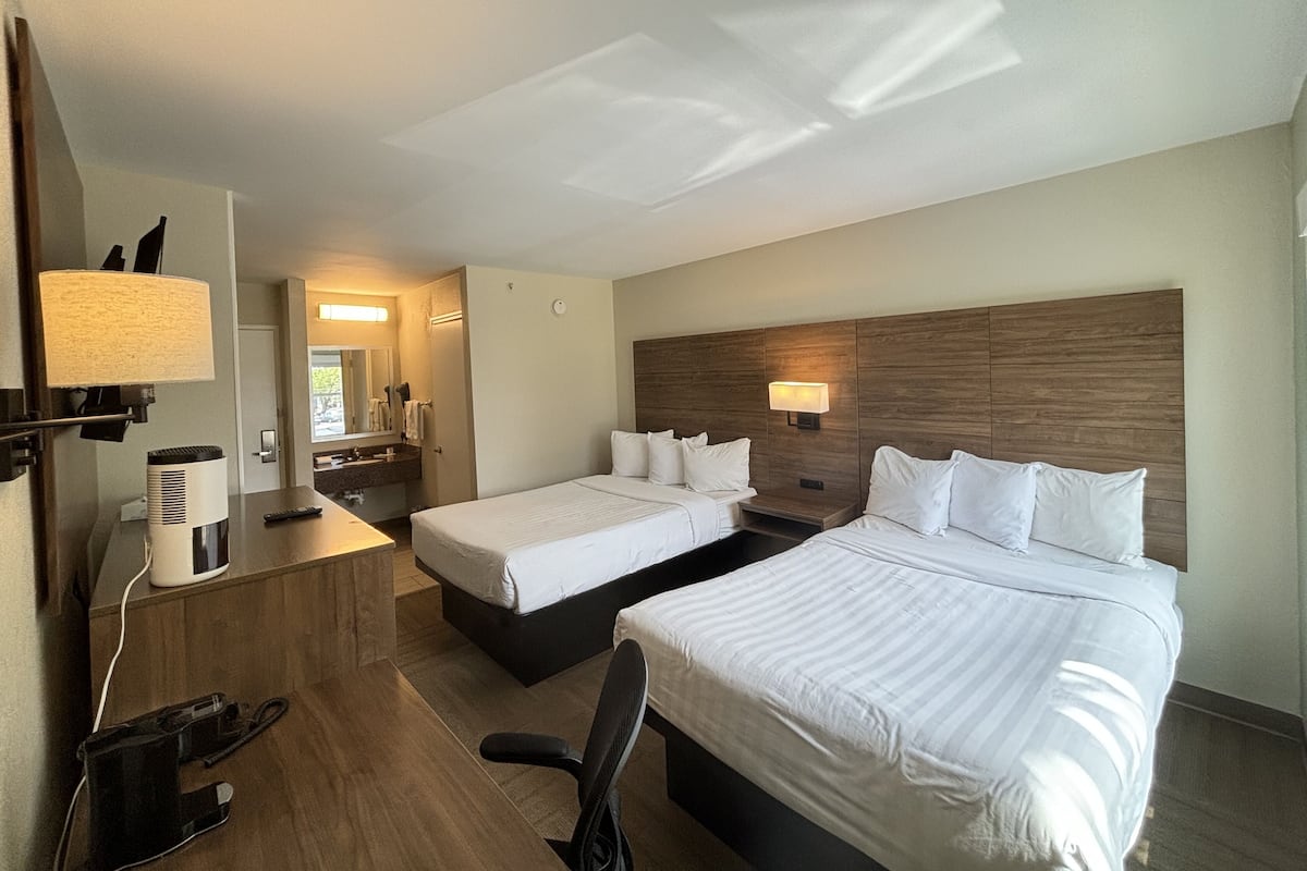 Une chambre d’hôtel avec deux lits, un bureau, une chaise, une lampe et un miroir.
