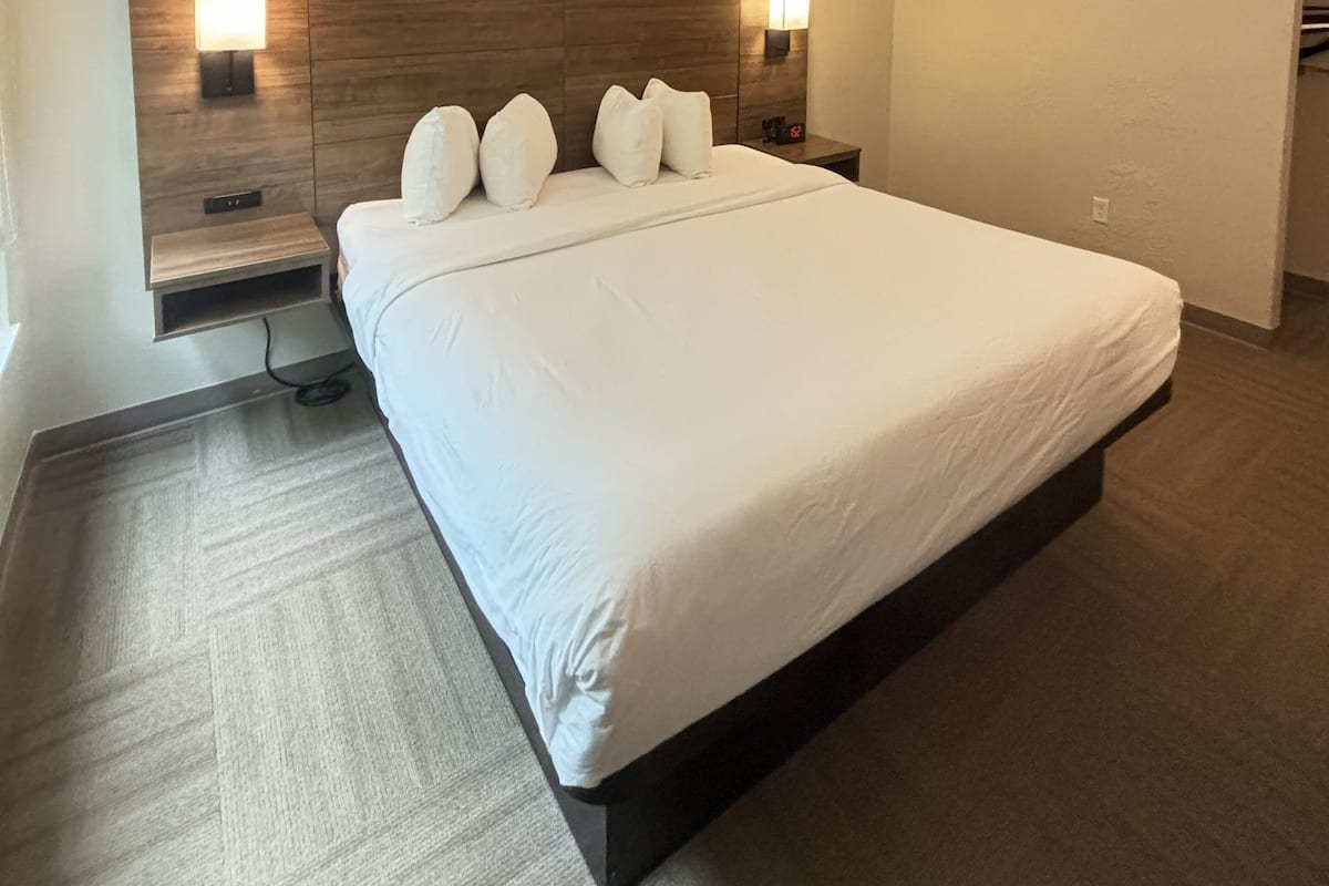 Une chambre d’hôtel moderne avec un grand lit, une tête de lit en bois, des lampes de chevet et un sol recouvert de moquette.