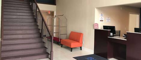 A hotel reception area with a staircase, a reception desk, and a red chair.