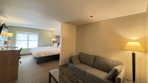 A hotel room with a bed, a sofa, a desk with a lamp, and a window. - Baymont by Wyndham Lake Park Valdosta I-75 (Lake Park)