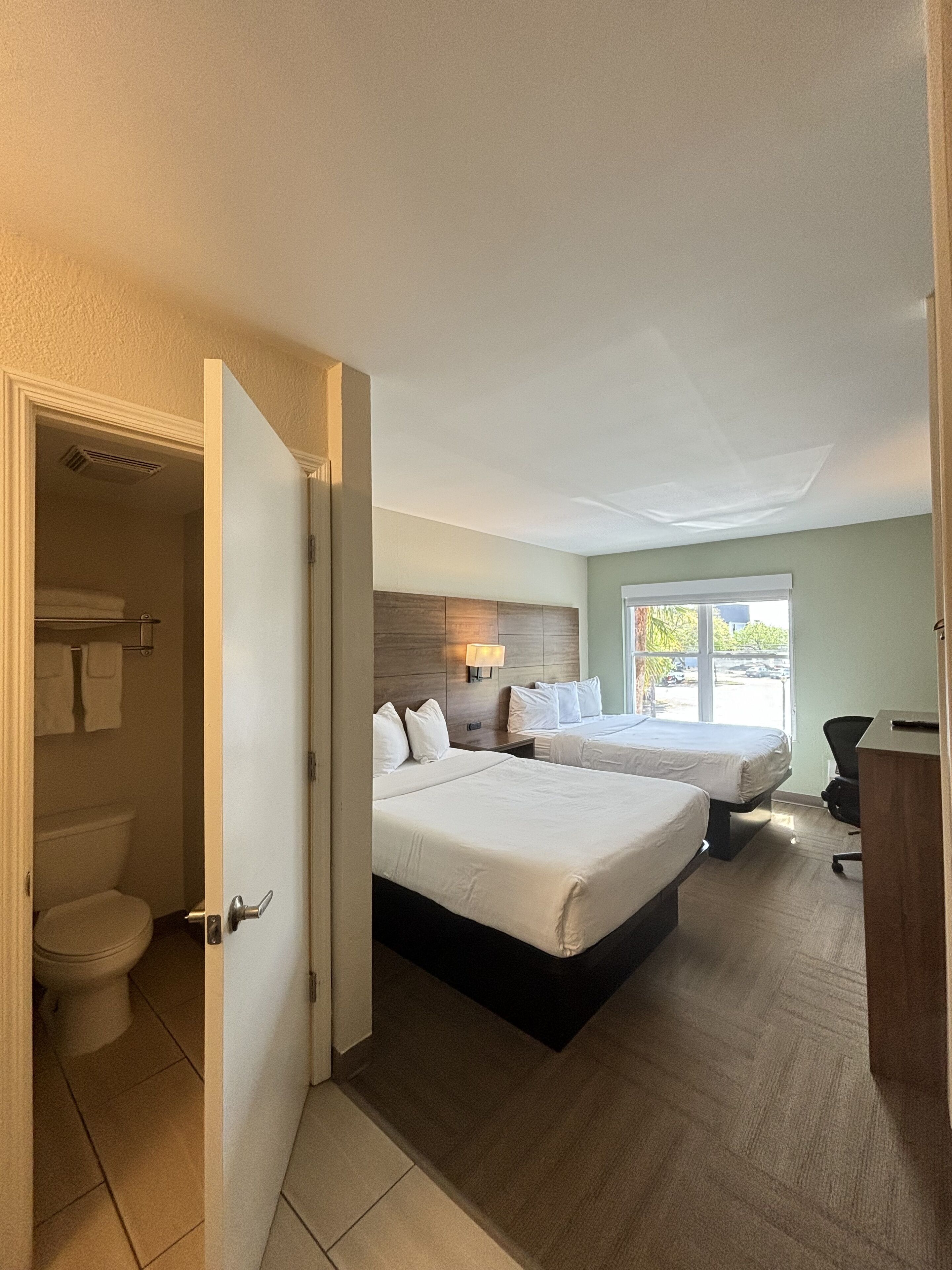Une chambre d’hôtel avec deux lits, un bureau, une chaise, une fenêtre et une salle de bain.