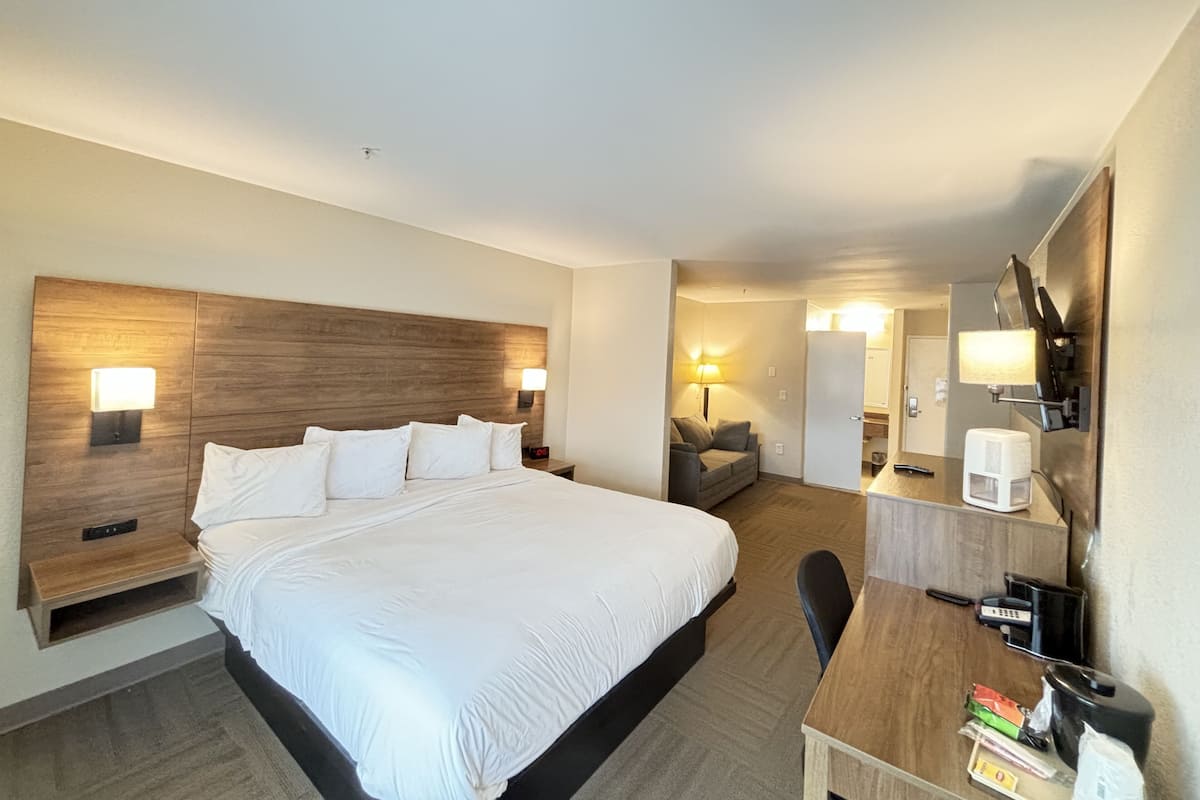 Une chambre d’hôtel avec un grand lit, des tables de chevet avec des lampes, un bureau avec une machine à café et un miroir.