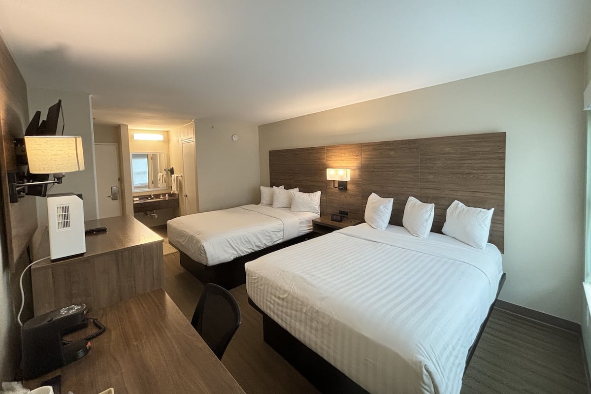 Une chambre d’hôtel avec deux lits, un bureau, une chaise, un miroir et une lampe.