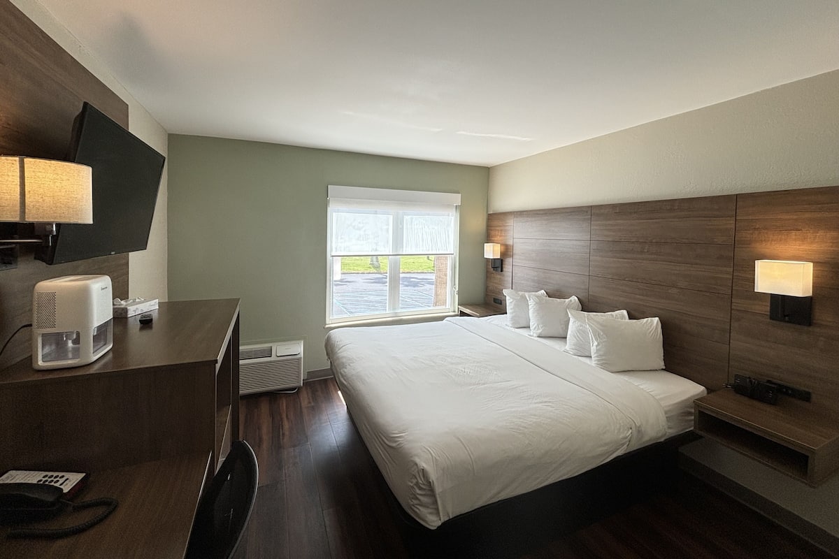Une chambre d’hôtel avec un grand lit, un bureau avec une lampe, un téléviseur à écran plat et une fenêtre donnant sur l’extérieur.