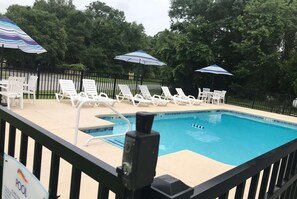 A swimming pool with white lounge chairs and striped umbrellas, surrounded by a black fence and trees. - Baymont by Wyndham Lake Park Valdosta I-75 (Lake Park)