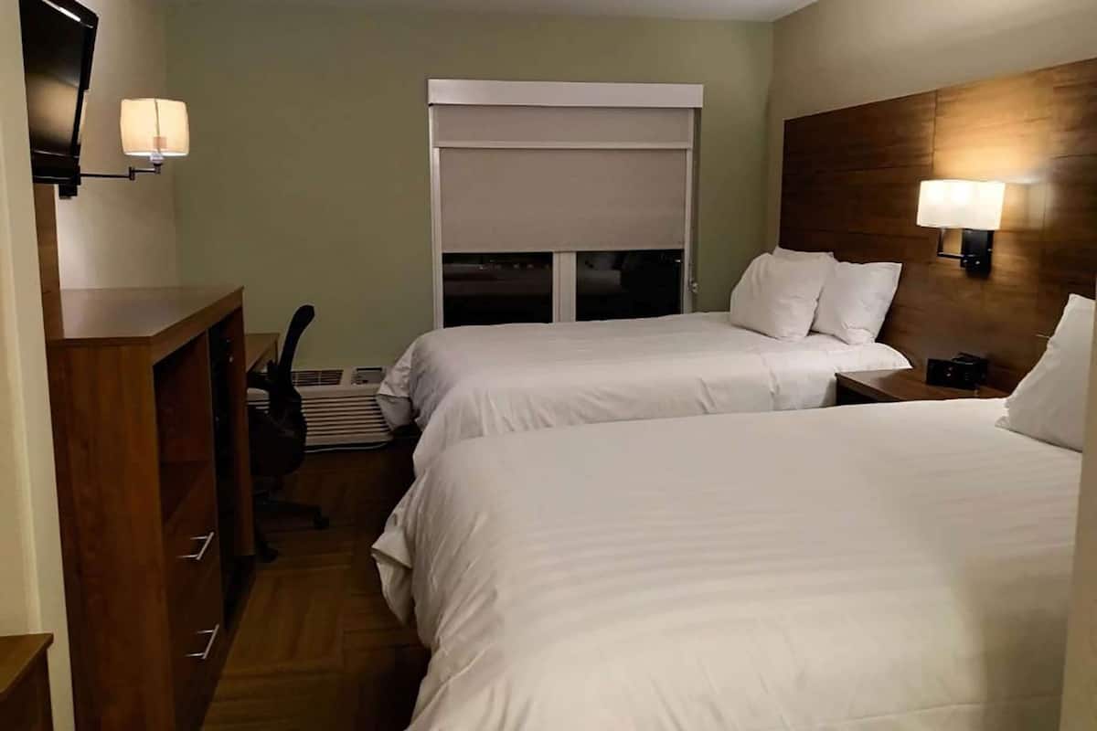 Une chambre d’hôtel avec deux lits, un bureau, une chaise, une télévision et une fenêtre avec un store.