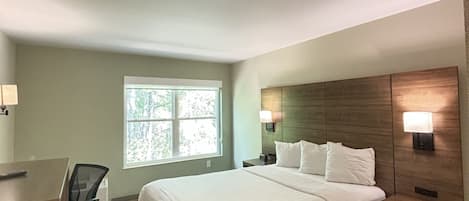 A hotel room with a bed, desk, chair, and a window with a view of trees.