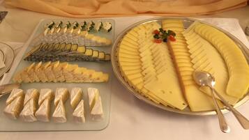 Un tavolo da buffet con diversi formaggi e un grande piatto di formaggio giallo a fette.
