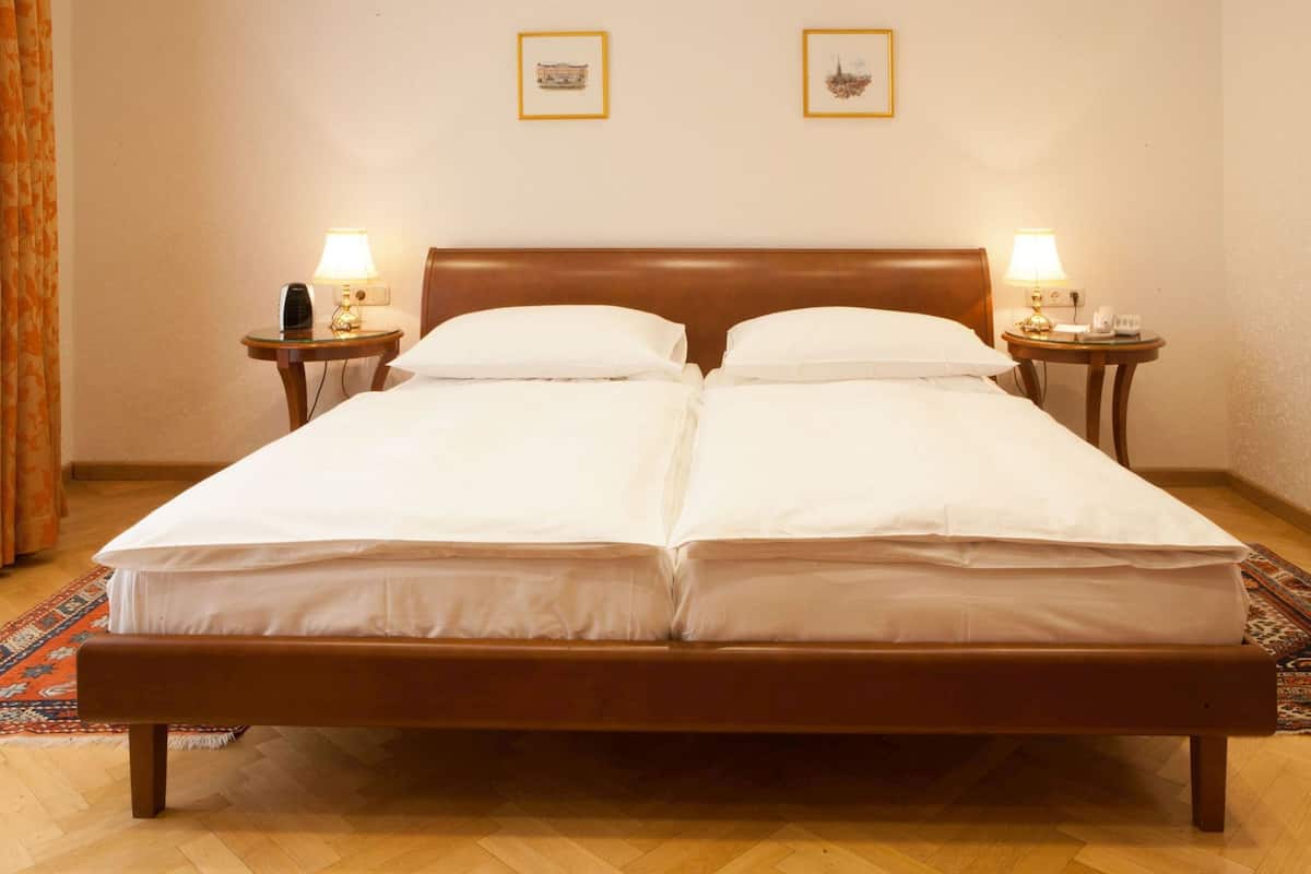 A double bed with a wooden frame, two bedside tables with lamps, and two framed pictures on the wall.