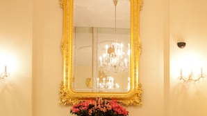 Una habitación con un espejo grande y ornamentado, una chimenea con un arreglo floral y una araña.