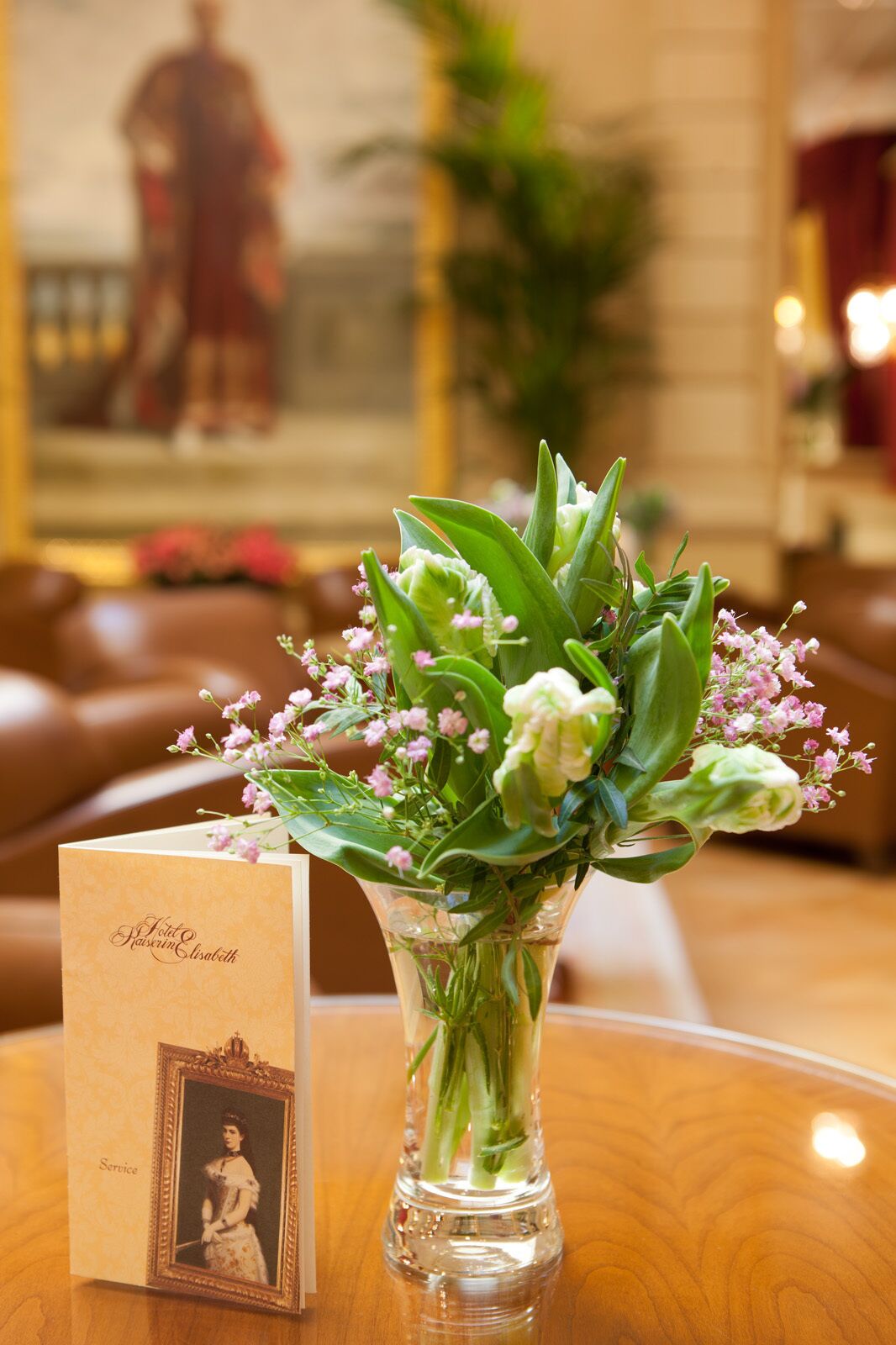 A table with a clear glass vase containing a bouquet of flowers and a card with a photo and name.