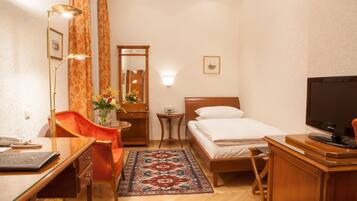 Une chambre d’hôtel comprenant un lit, un bureau avec une lampe, une chaise, une télévision, une petite table avec un vase de fleurs et un miroir.