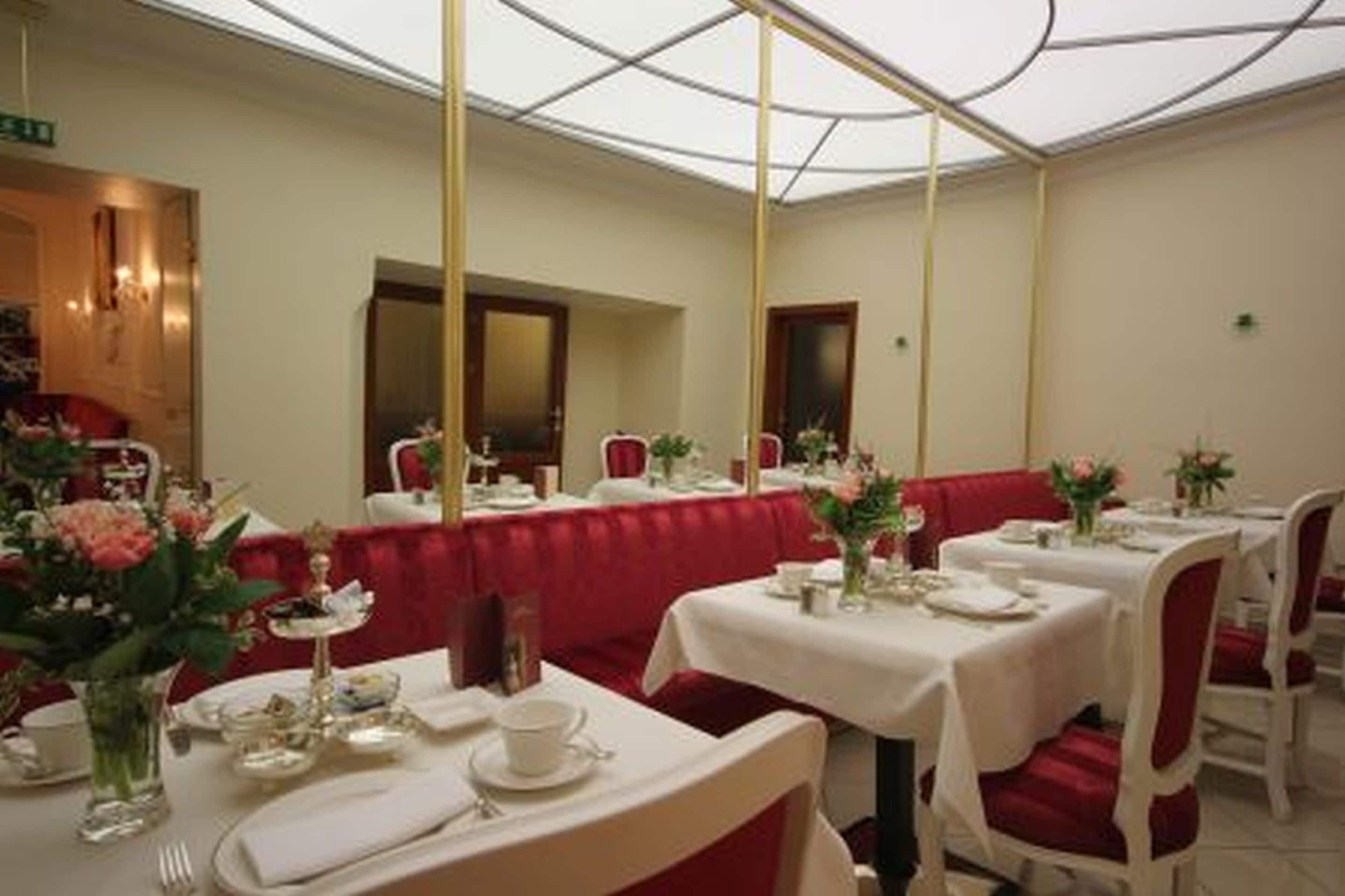 Un espace repas avec des tables dressées, des chaises à revêtement rouge et un plafond en verre.