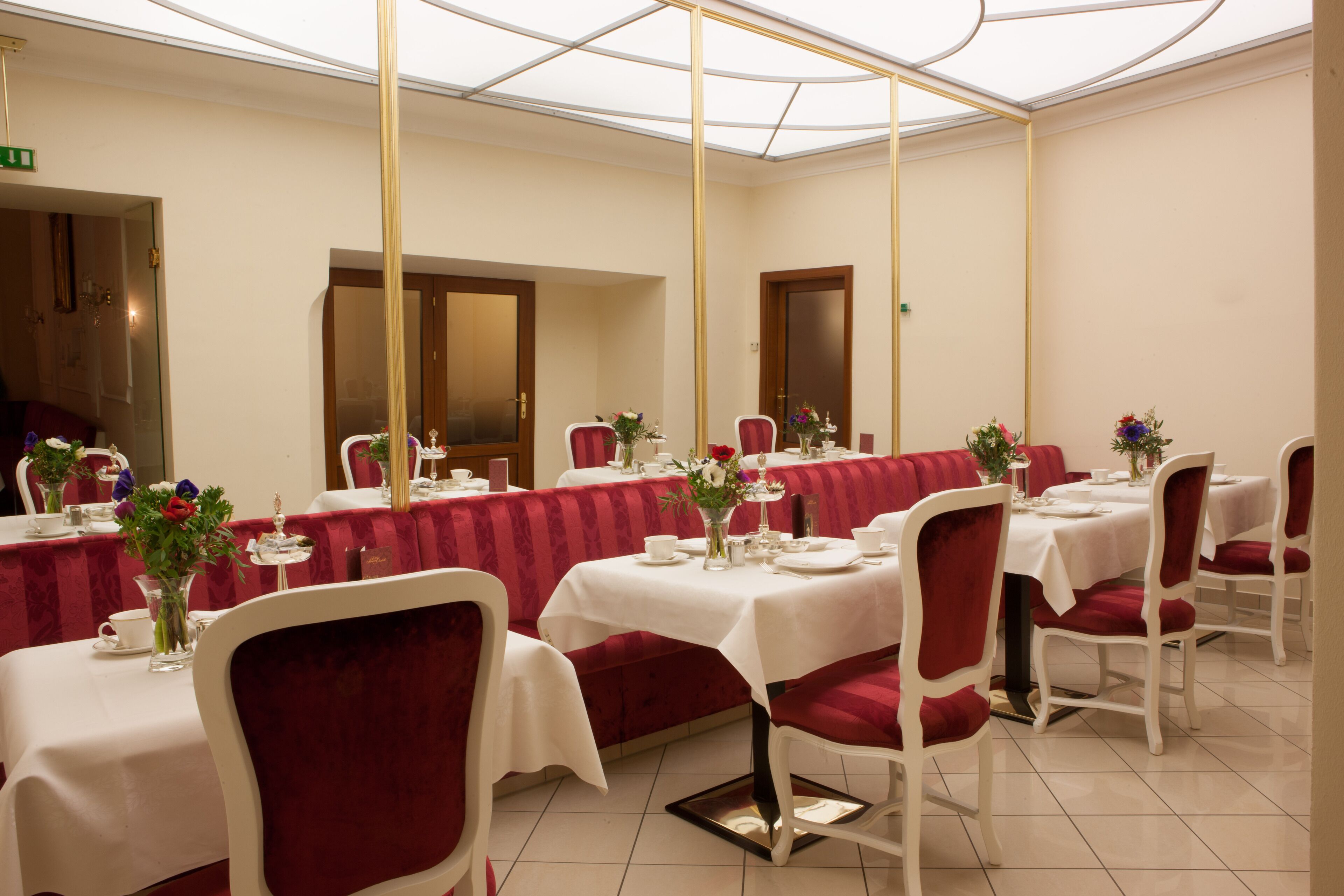A formal dining area with tables set for service, red upholstered chairs, and a glass ceiling.