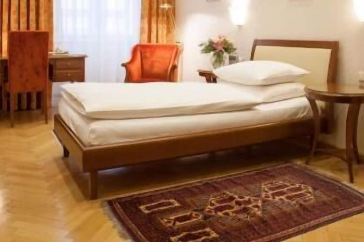 A hotel room with a bed, a chair, a nightstand, a desk, and a window with curtains.