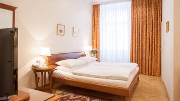 A hotel room with a bed, a TV, a lamp, and a window with curtains.