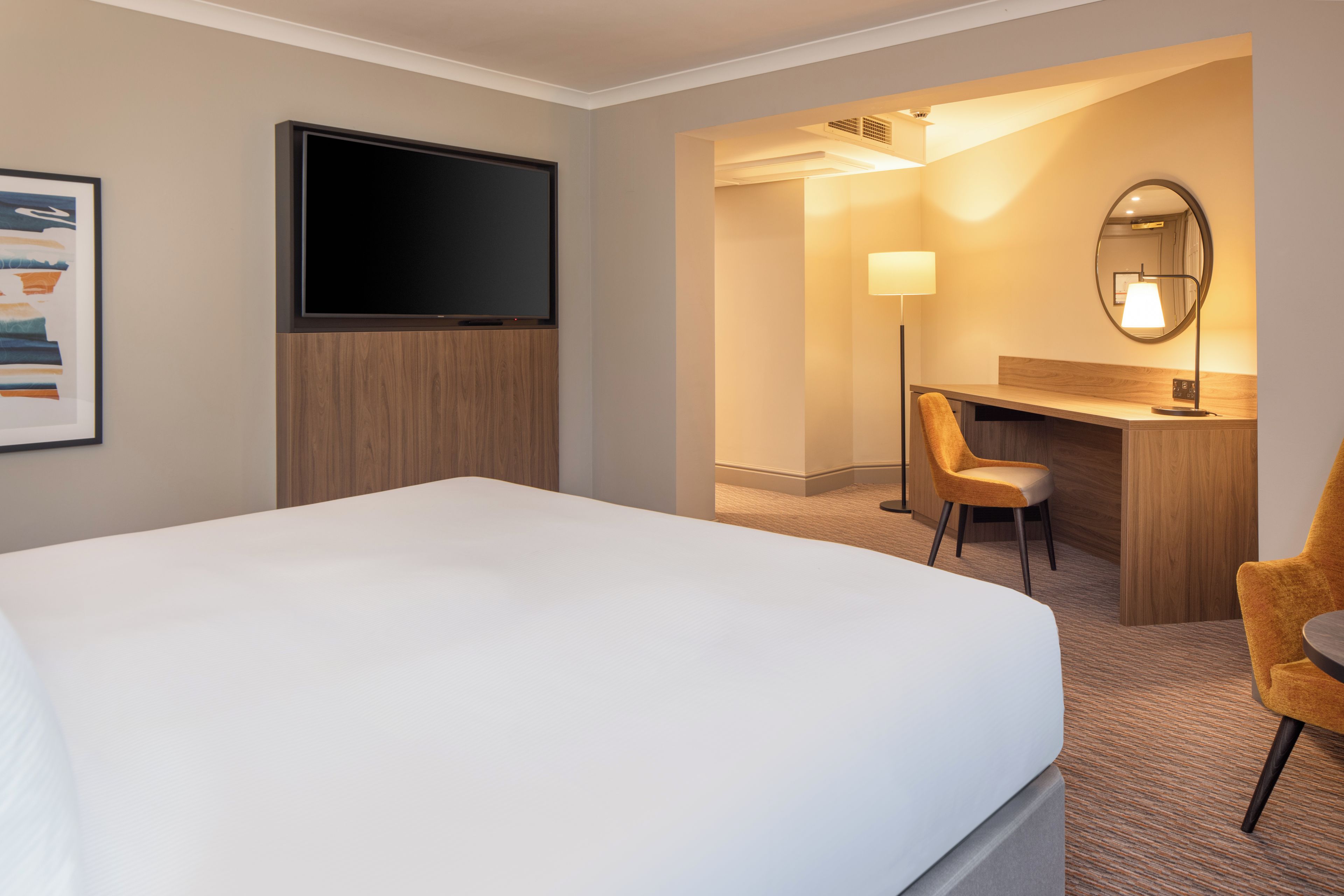 A hotel room with a bed, a desk, a chair, a television, and a lamp.