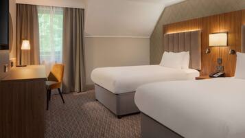 A hotel room with two beds, a desk, a chair, and a TV.