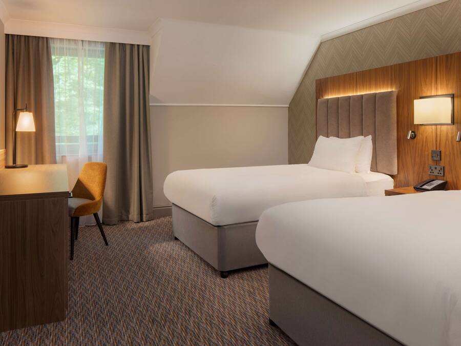 A hotel room with two beds, a desk, a chair, and a TV.