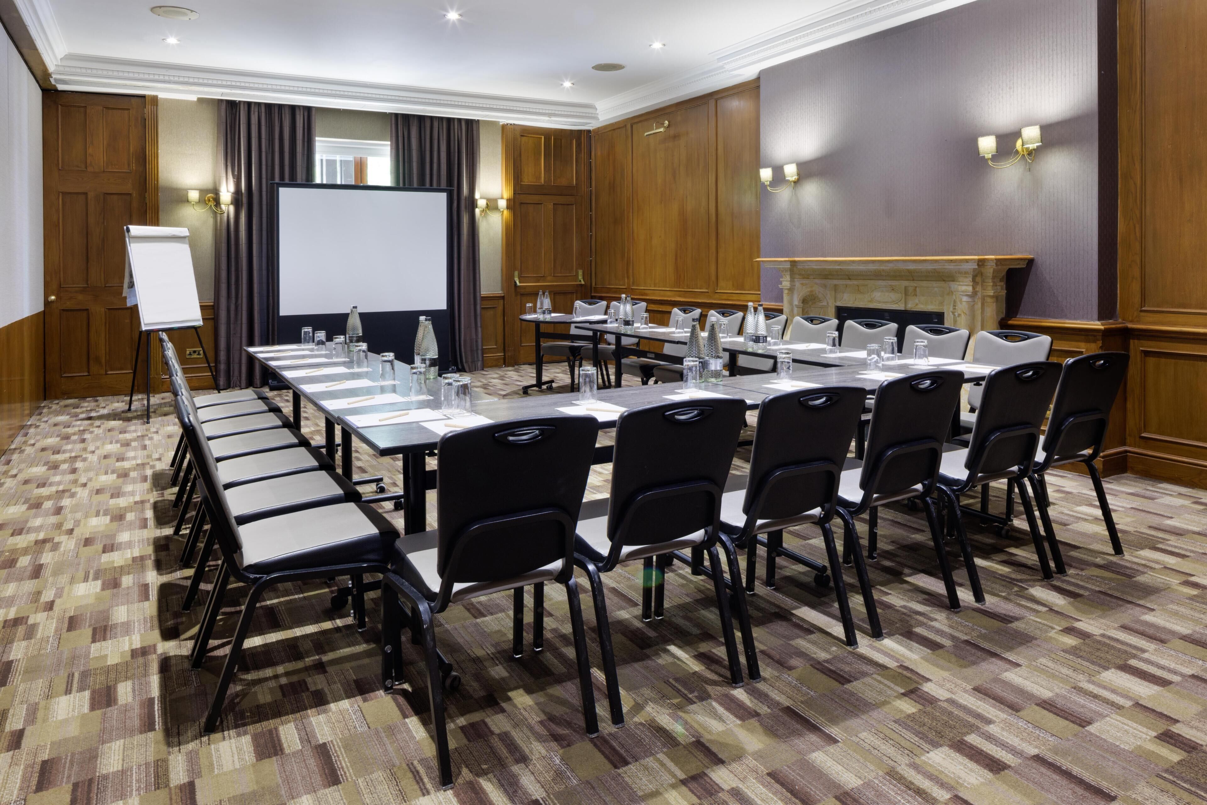 A conference room with a long table, chairs, a whiteboard, and a projection screen.