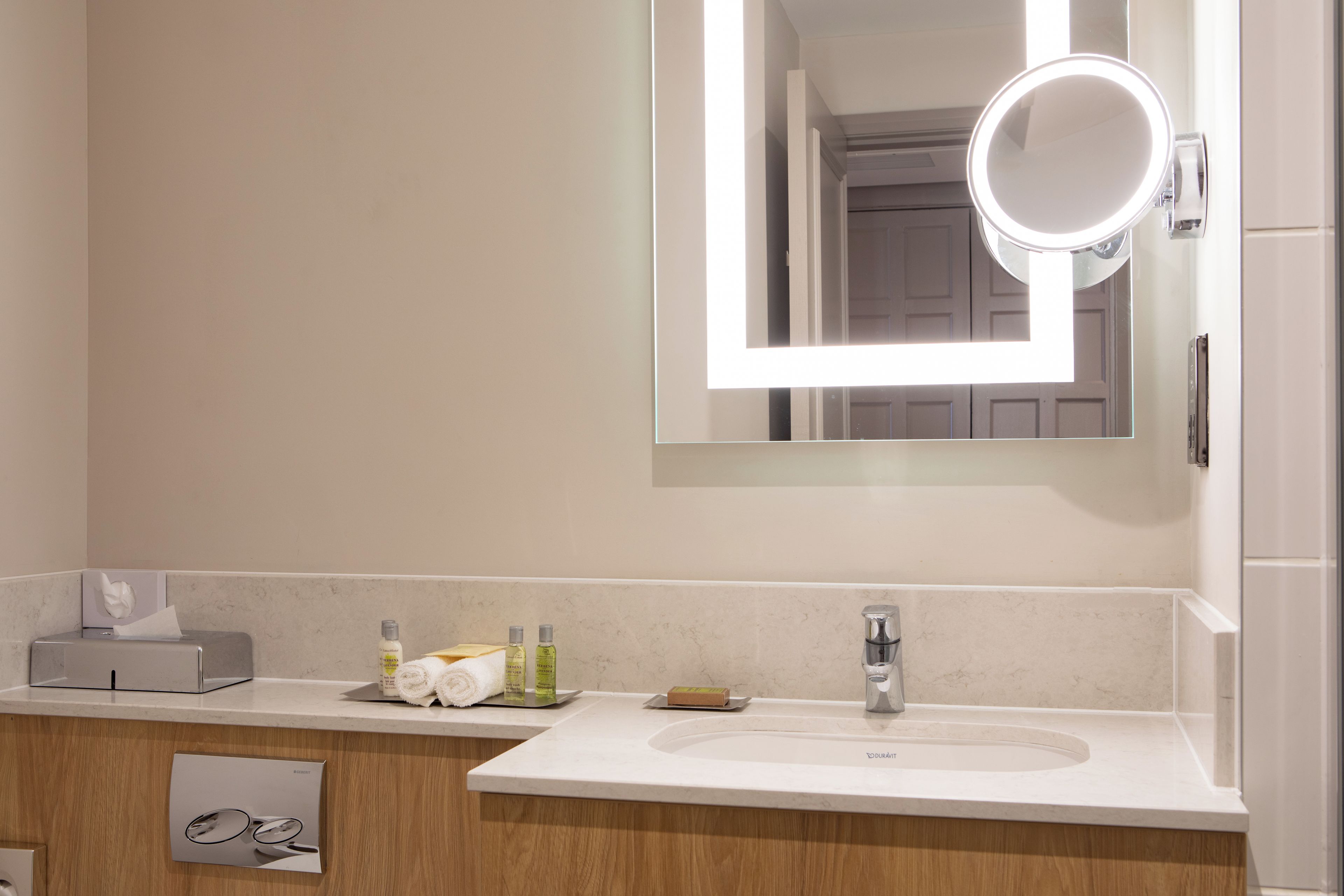 A modern bathroom with a white sink, mirror, and a wooden vanity.