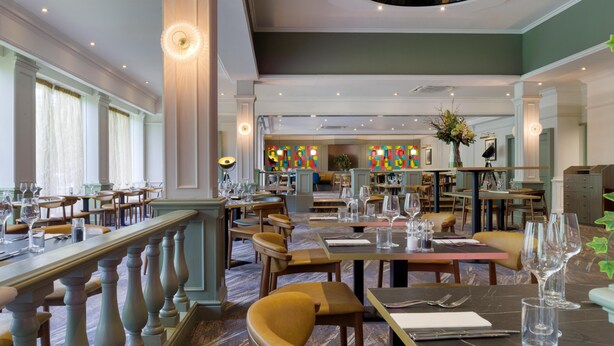 A restaurant with multiple dining tables and chairs, a staircase, and a view of the dining area.