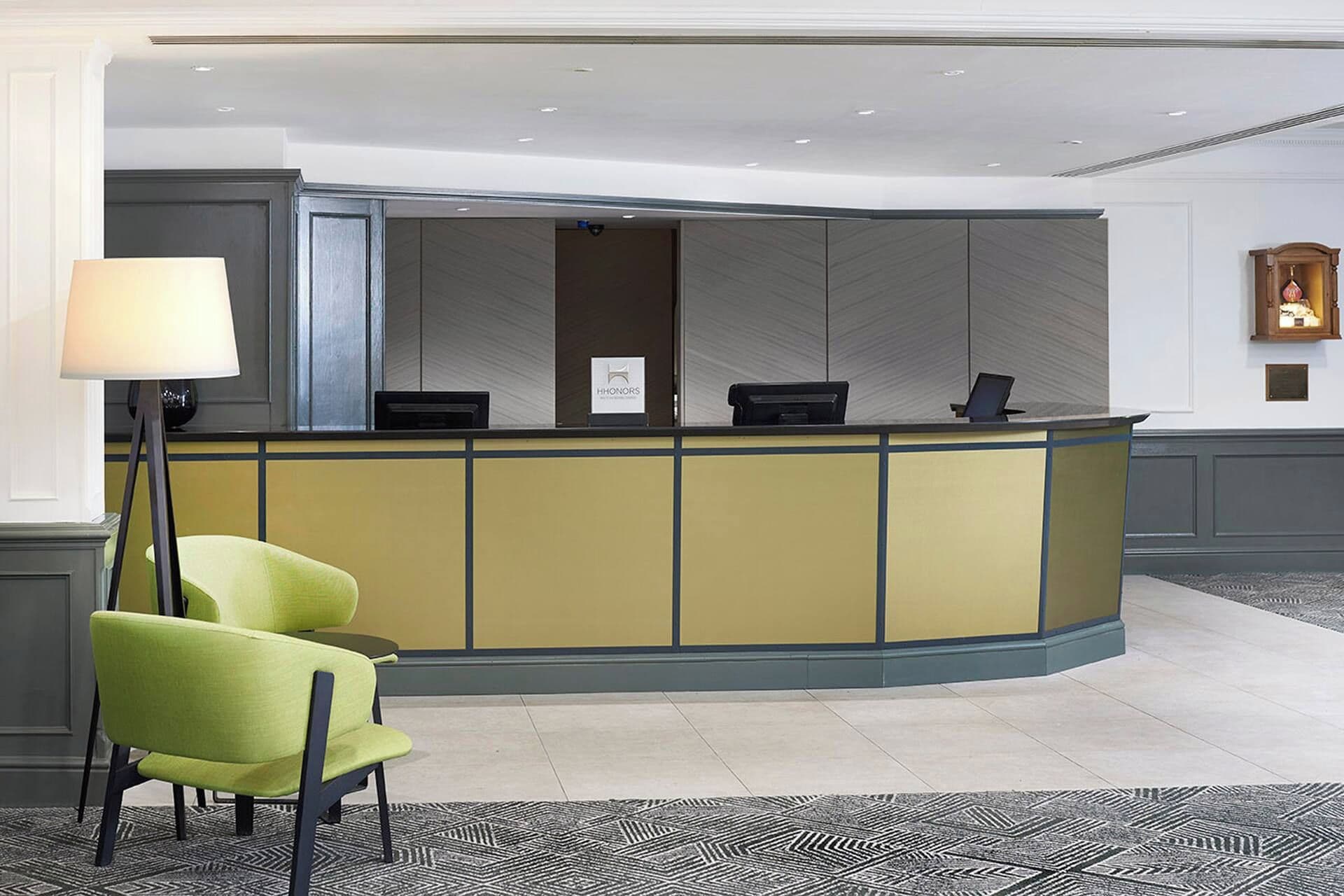 A reception desk with a yellow and blue color scheme, a green chair, and a floor lamp.