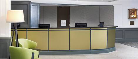 A reception desk with a yellow and blue color scheme, a green chair, and a floor lamp.