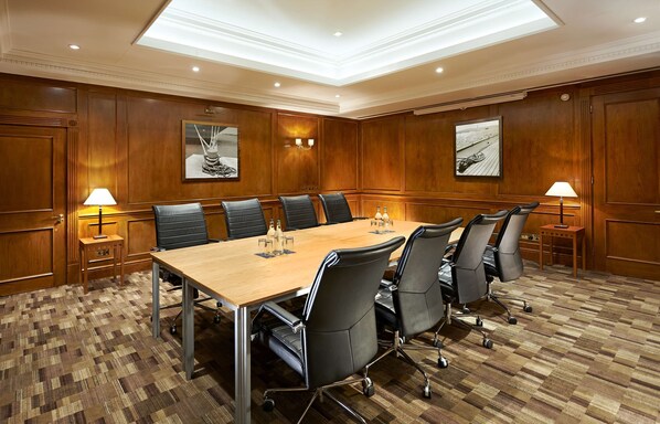 A conference room with a large wooden table, six black chairs, two wall-mounted lamps, and two framed pictures on the walls. - DoubleTree by Hilton Southampton (Southampton)