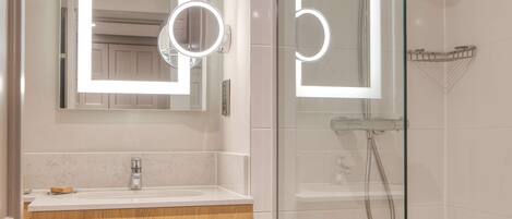 A modern bathroom with a glass-enclosed shower, a vanity with a mirror and lights, and neatly folded towels.
