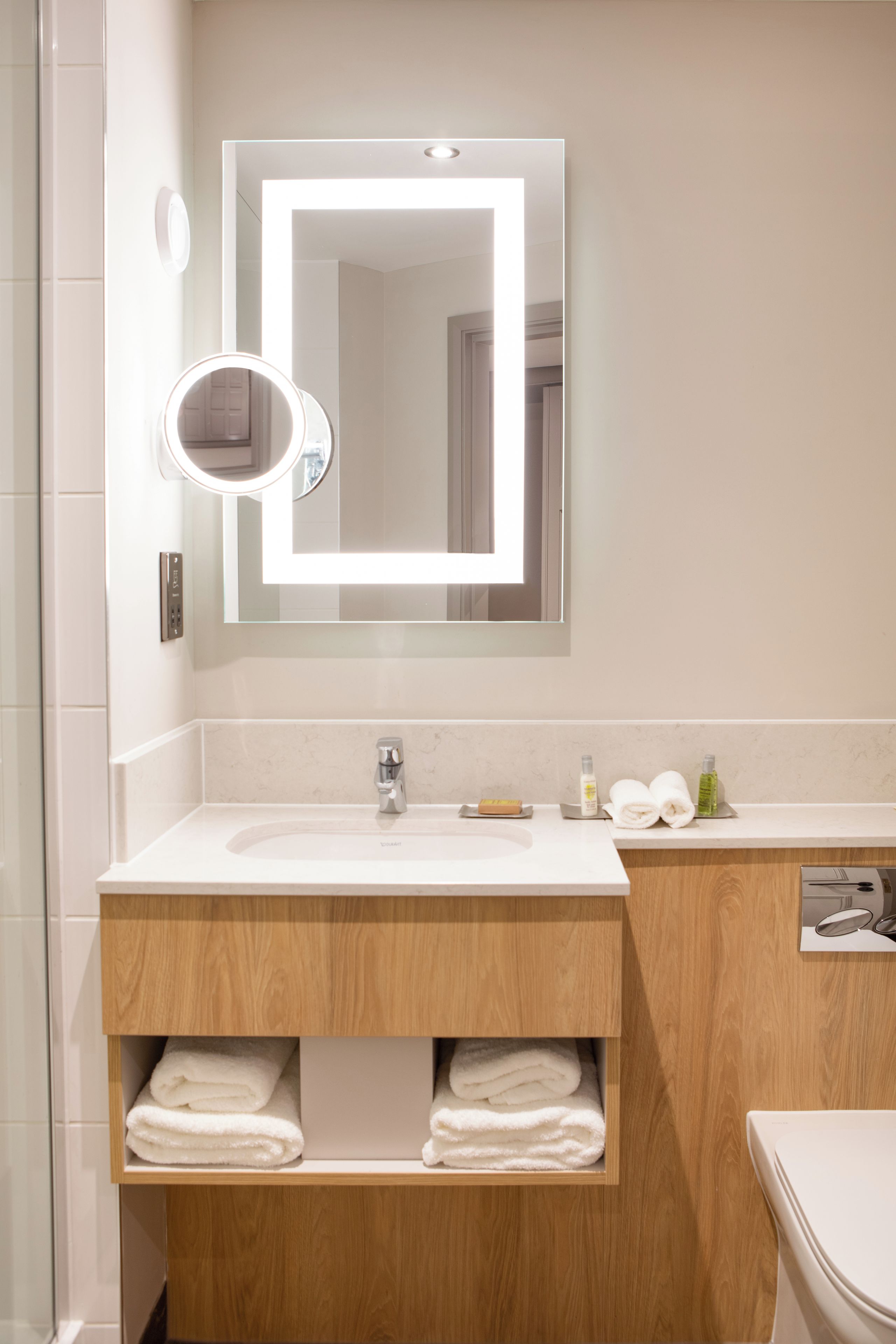 A modern bathroom with a vanity, mirror, and built-in shelves for towels.