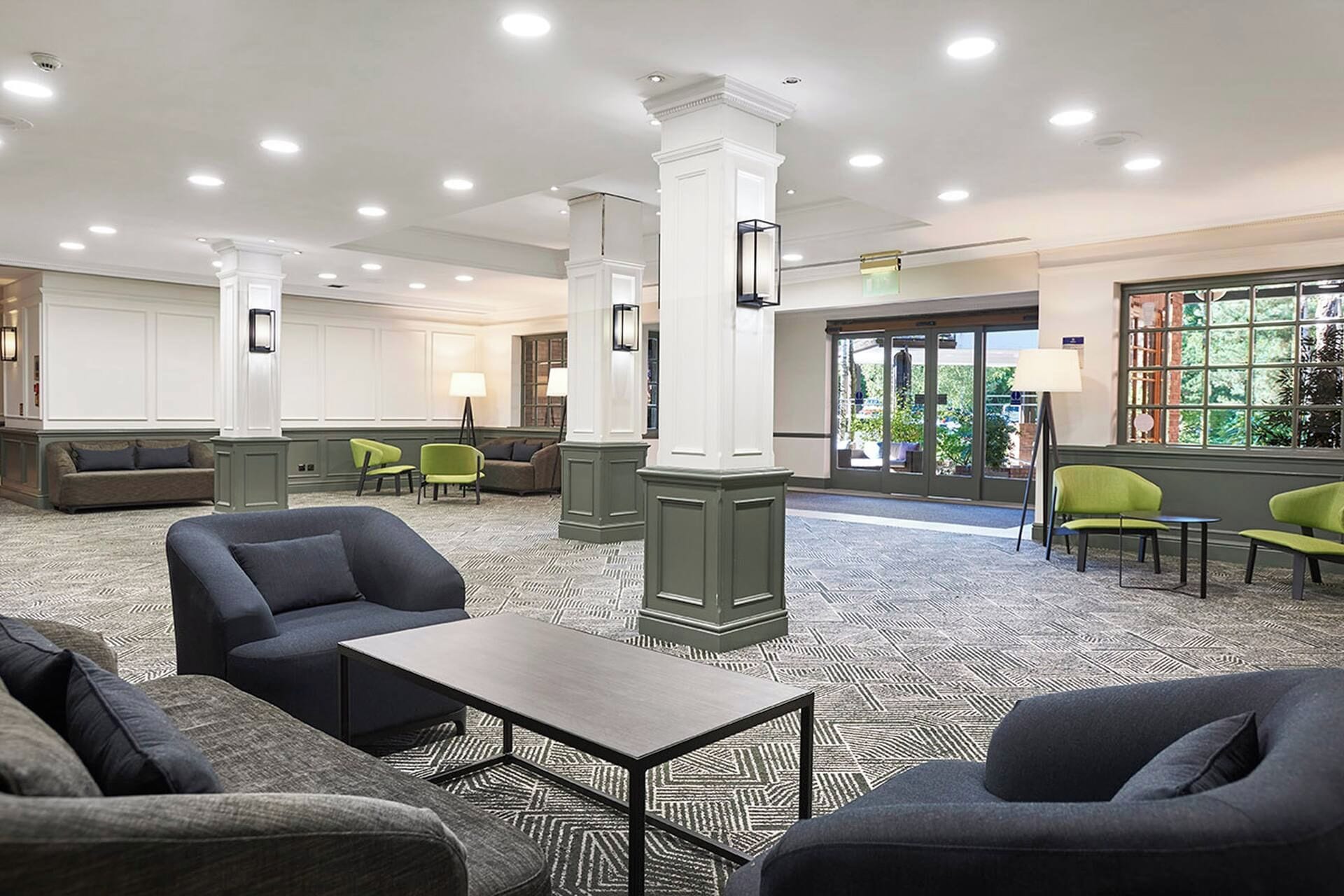 A hotel lobby with seating areas, a reception desk, and a large window providing a view of the outdoors.
