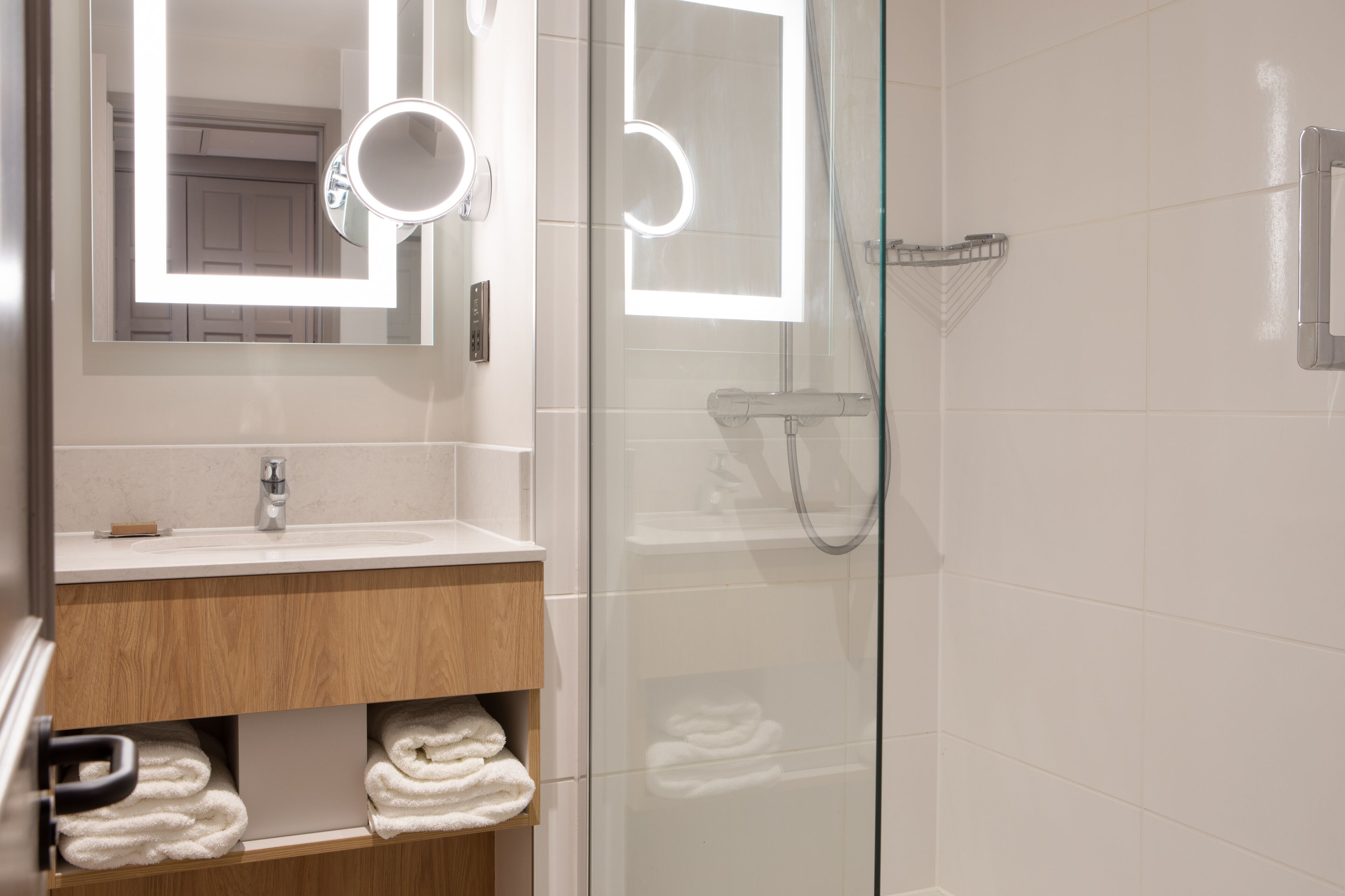 A modern bathroom with a glass shower enclosure, a vanity with a mirror, and neatly folded towels.