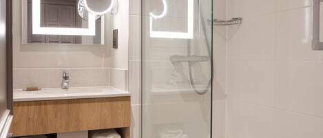 A modern bathroom with a glass shower enclosure, a vanity with a mirror, and neatly folded towels.