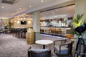 Un hall d’hôtel comprenant un bar, des espaces aménagés pour s’asseoir et une plante décorative.