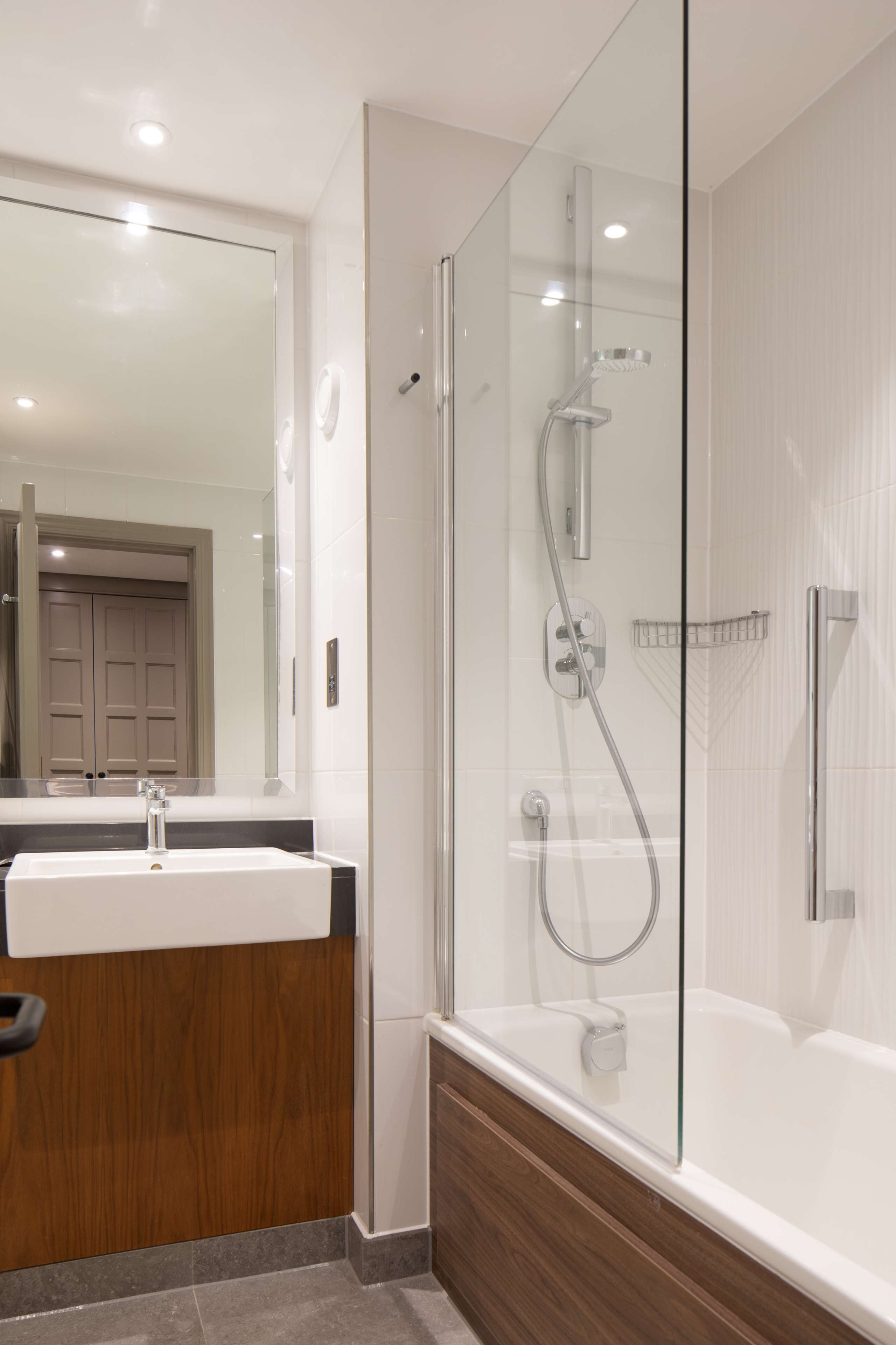 A modern bathroom with a glass-enclosed shower, a wooden vanity, and a large mirror.