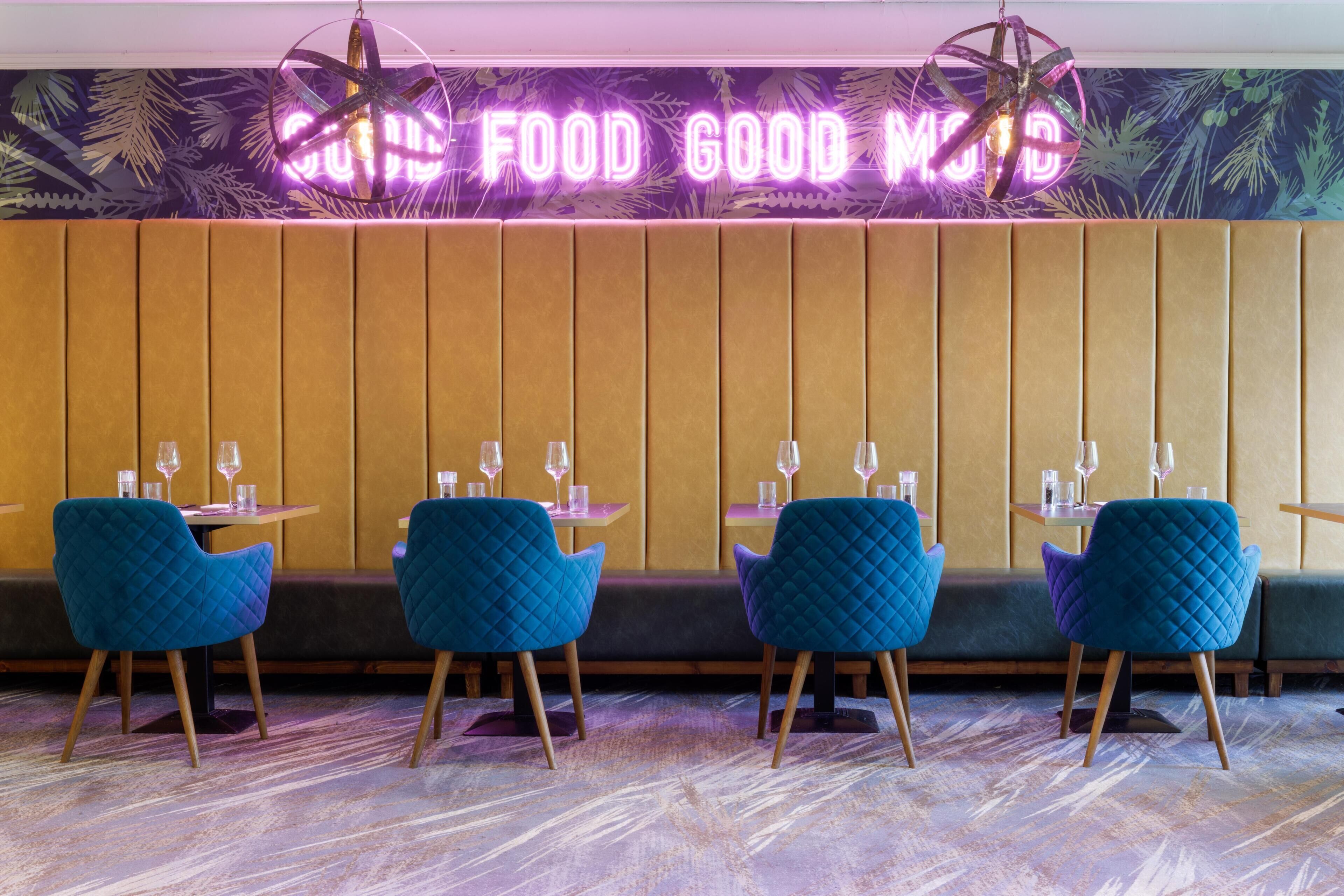 L’intérieur d’un restaurant avec un panneau néon, des chaises bleues et un mur orné de motifs.