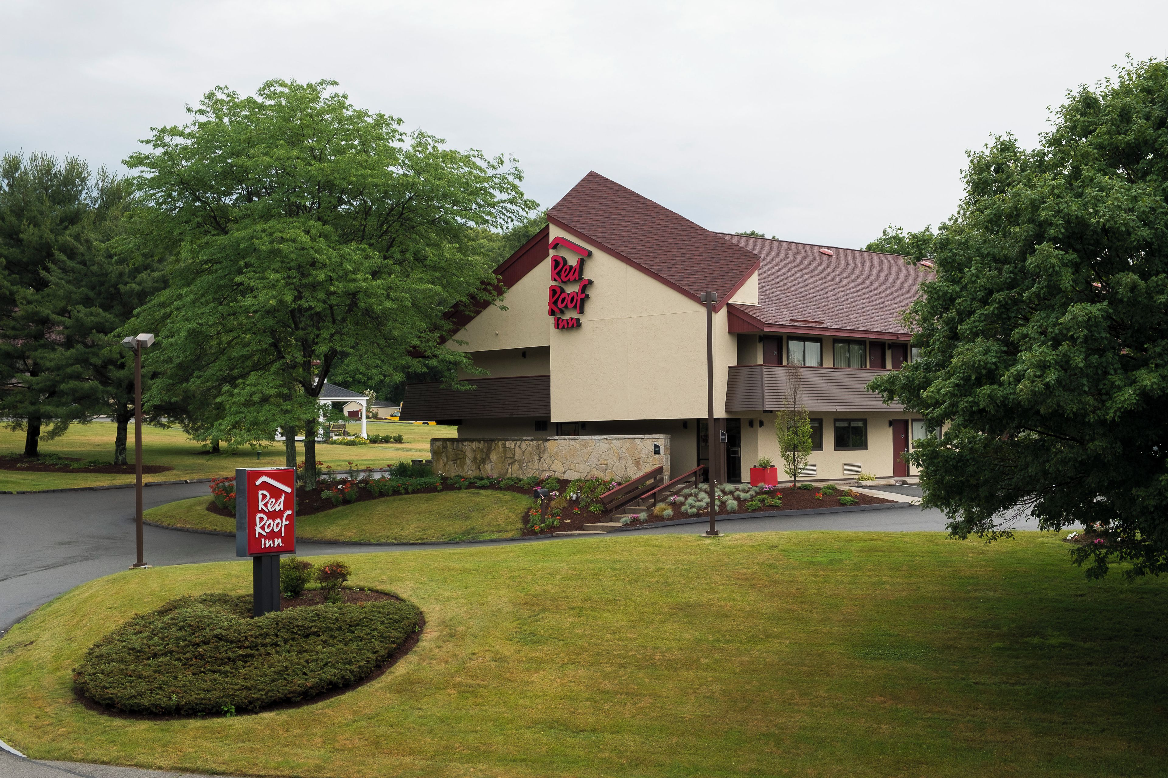 A Red Roof Inn with a two-story structure, a stone facade, and a landscaped front yard.