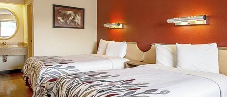 A hotel room with two beds, a bathroom with a round mirror, and a wall-mounted light fixture.