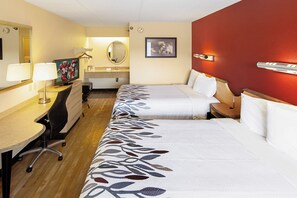 A hotel room with two beds, a desk with a chair, a television, and a bathroom with a mirror.