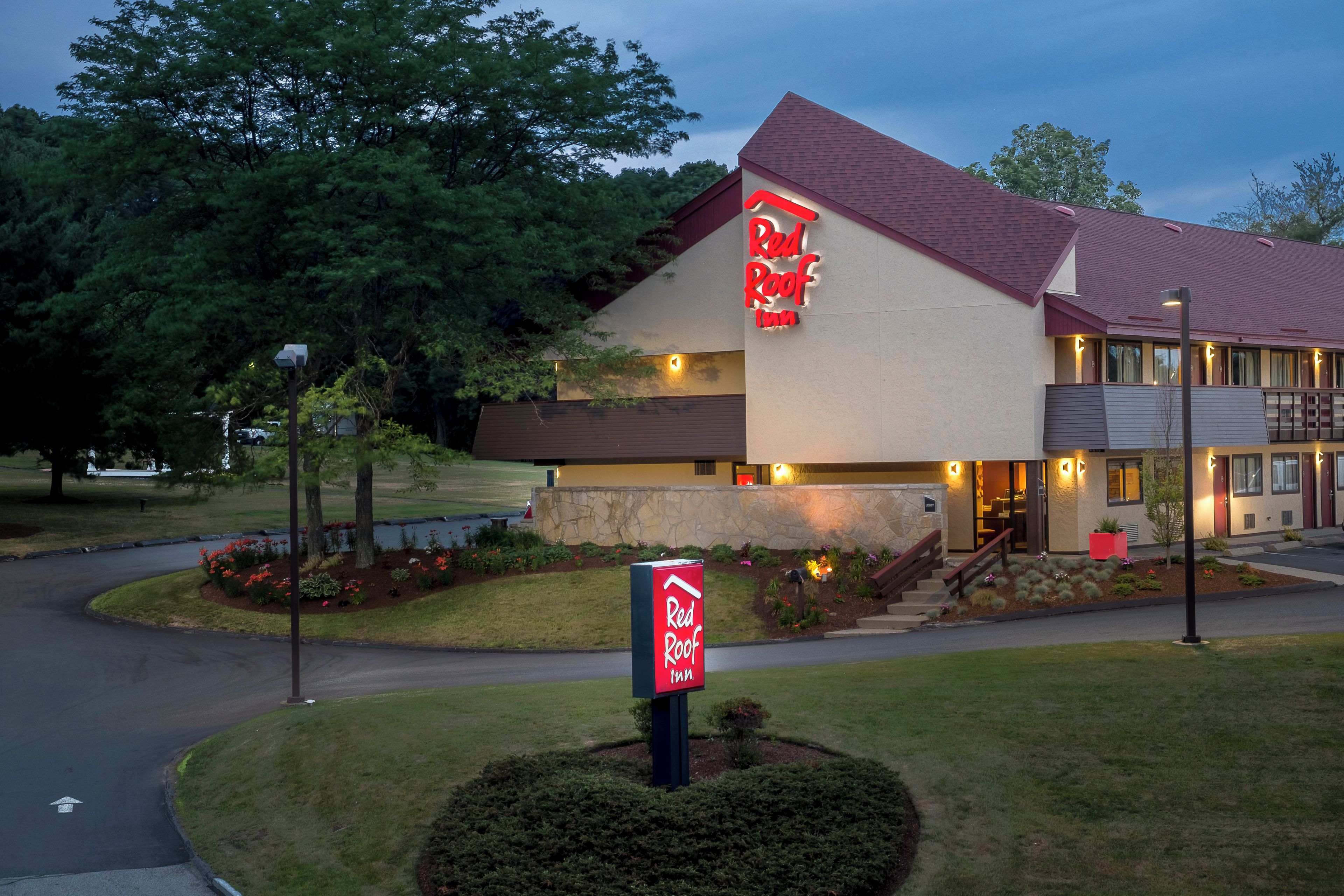 Ett Red Roof Inn-hotell med en fasad av sten, ett rött tak och en väl upplyst entré.