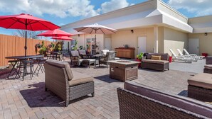 Une terrasse extérieure avec des meubles en osier, des parasols rouges et un sol en briques.