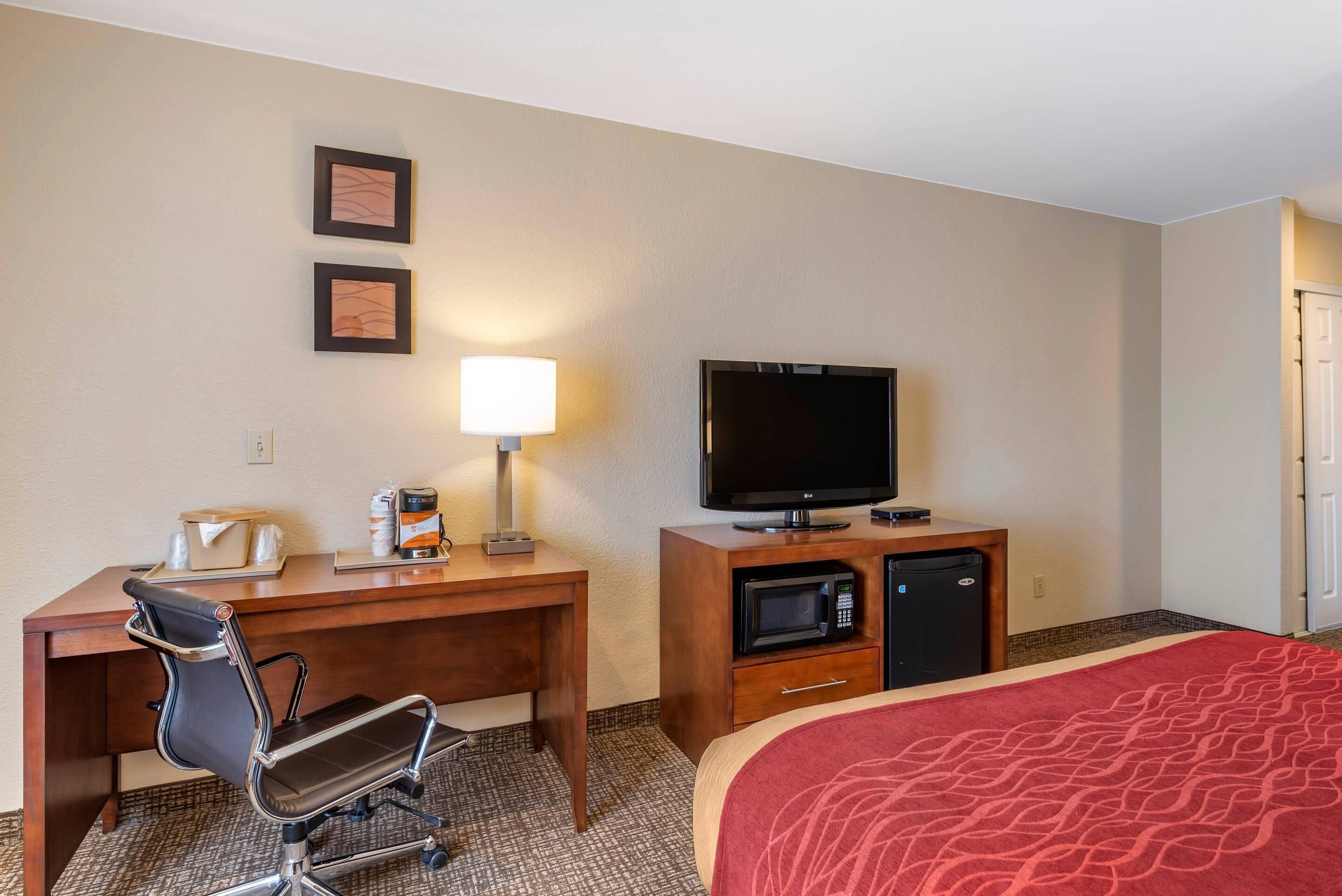 A hotel room with a bed, a desk with a chair, a television, a microwave, and a coffee maker.