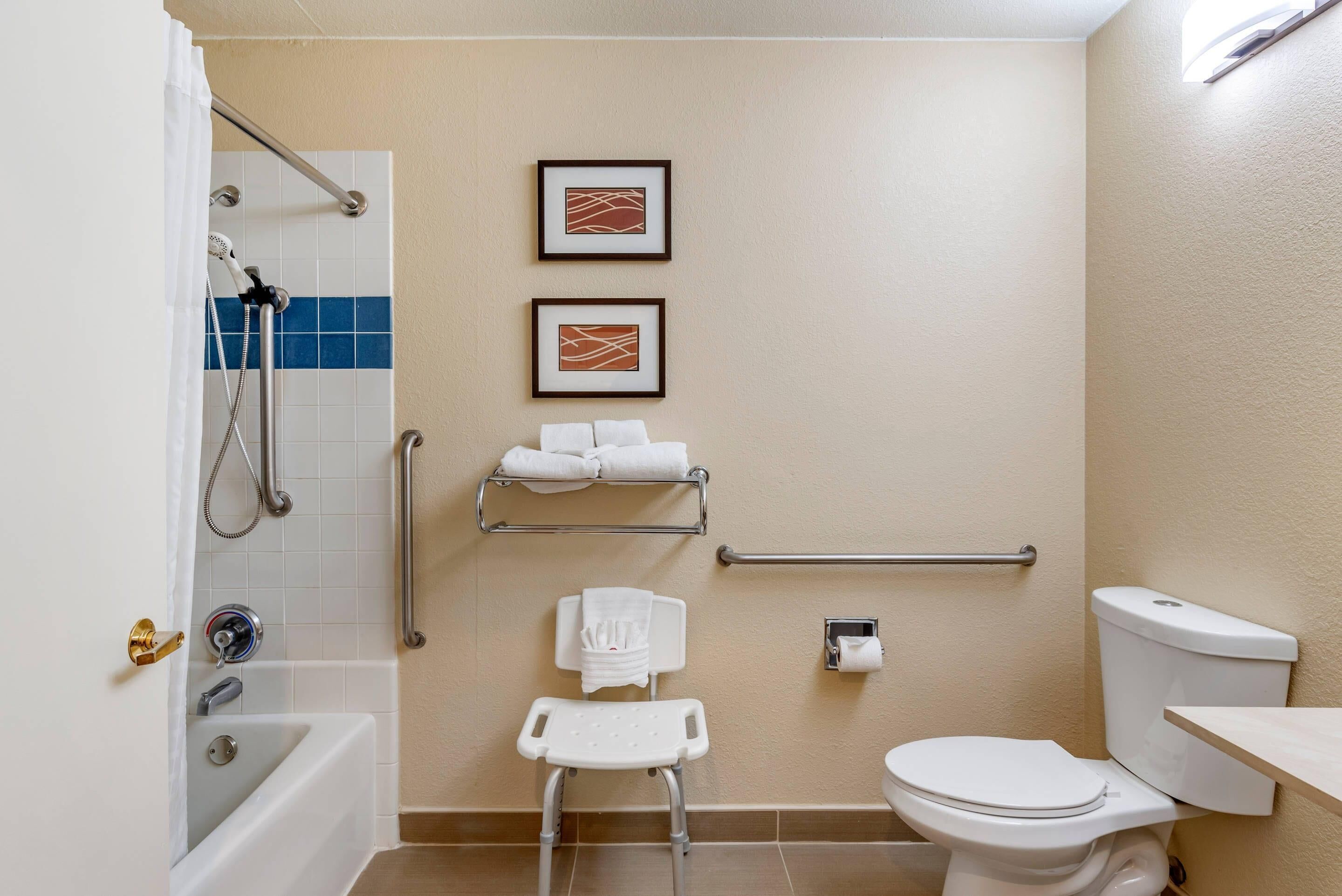 Une salle de bain équipée d’une douche, de toilettes, de barres d’appui et d’une petite chaise blanche.