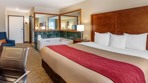 Une chambre d’hôtel avec un grand lit, un coin salon avec un fauteuil, une salle de bain avec une baignoire et un miroir.