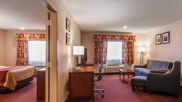 A hotel room with a bed, a desk with a lamp, a chair, a sofa, and an air conditioning unit.