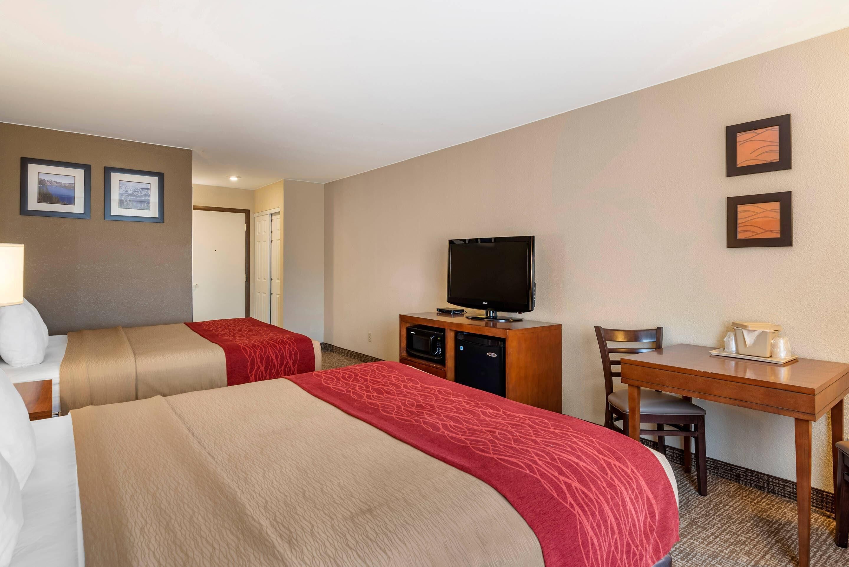 A hotel room with two beds, a desk, a television, and a microwave.