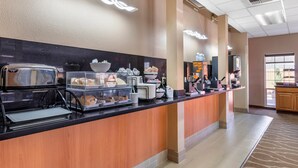Un espace pour le petit-déjeuner à l’hôtel, équipé d’un buffet où les clients peuvent se servir eux-mêmes, comprenant une machine à café, des bols et des plateaux.